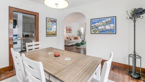 Un coin repas avec une table en bois et des chaises blanches, une cuisine en arrière-plan et une carte encadrée accrochée au mur.