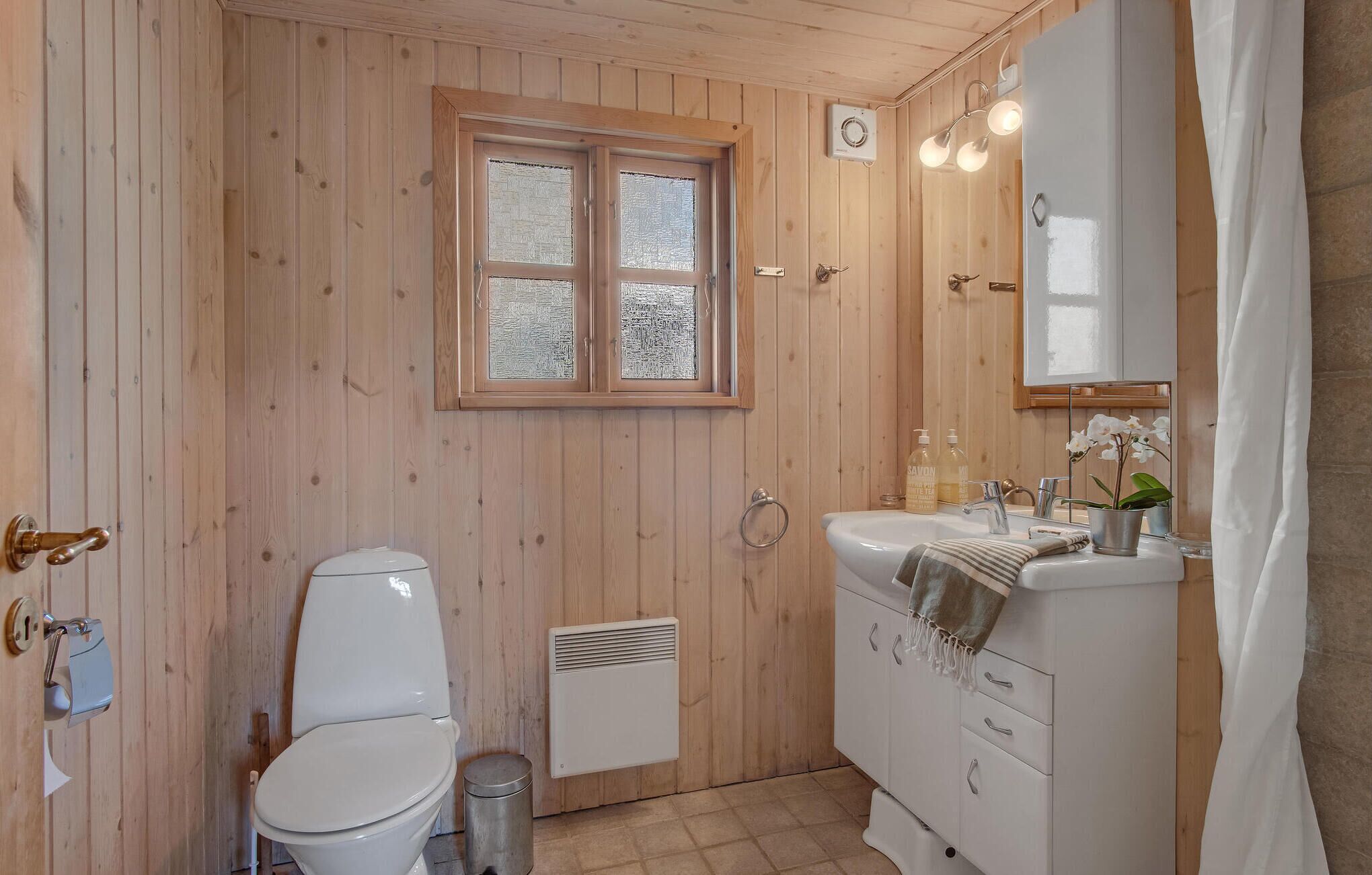 A wooden-paneled bathroom with a toilet, sink, and window.