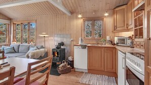 A cozy cabin interior with a wooden interior, a fireplace, a dining area, and a kitchen with modern appliances. - Stunning home in Fårevejle with WiFi (Fårevejle)