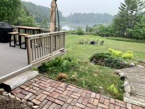 A deck with outdoor furniture overlooking a lake, surrounded by greenery and a stone wall. - Family friendly lakefront property on large wilderness estate with sandy beach (Land O' Lakes)