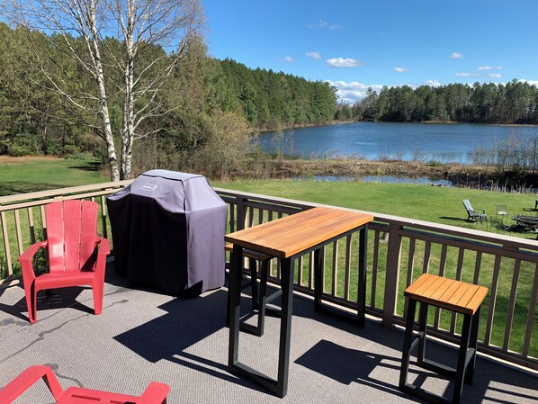 Une terrasse avec une table et des chaises, donnant sur un lac et une forêt.