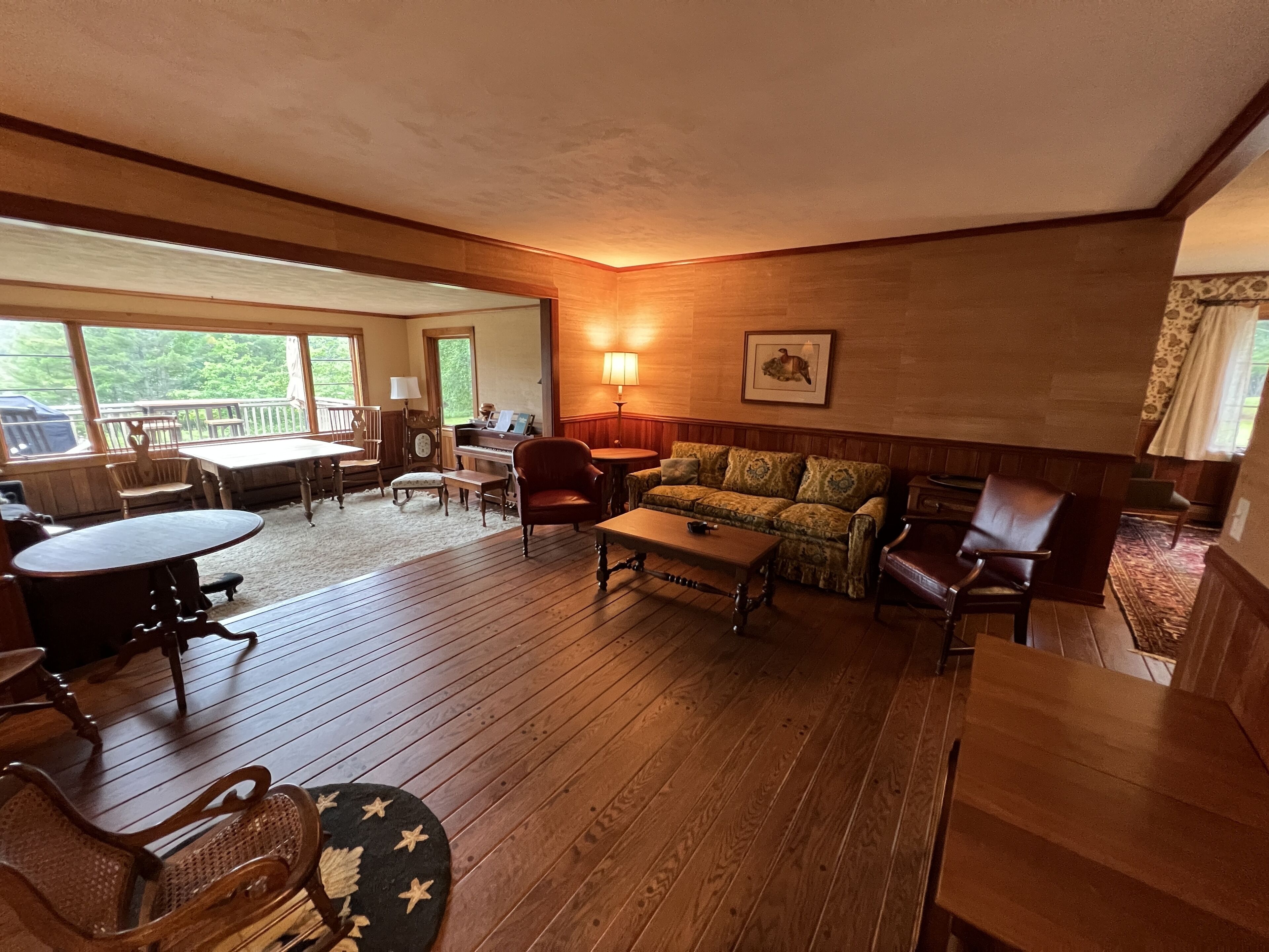 Een gezellige woonkamer met houten vloeren, een piano, een bank en een eettafel.