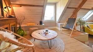 A cozy attic room with a wooden floor, a round wooden table, a wicker chair, a small bench, a green vase, a yellow cushion, a wooden swing, and a window with a view. - 3 bedroom stunning home in Saint-Brice-de-Landell (Saint-Brice-de-Landell)