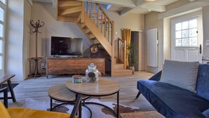A spacious living room with a blue sofa, a round wooden coffee table, a TV on a wooden cabinet, and a staircase leading to an upper floor. - 3 bedroom stunning home in Saint-Brice-de-Landell (Saint-Brice-de-Landell)