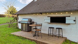 An outdoor barbecue area with a grill, a pizza oven, and two bar stools. - 3 bedroom stunning home in Saint-Brice-de-Landell (Saint-Brice-de-Landell)