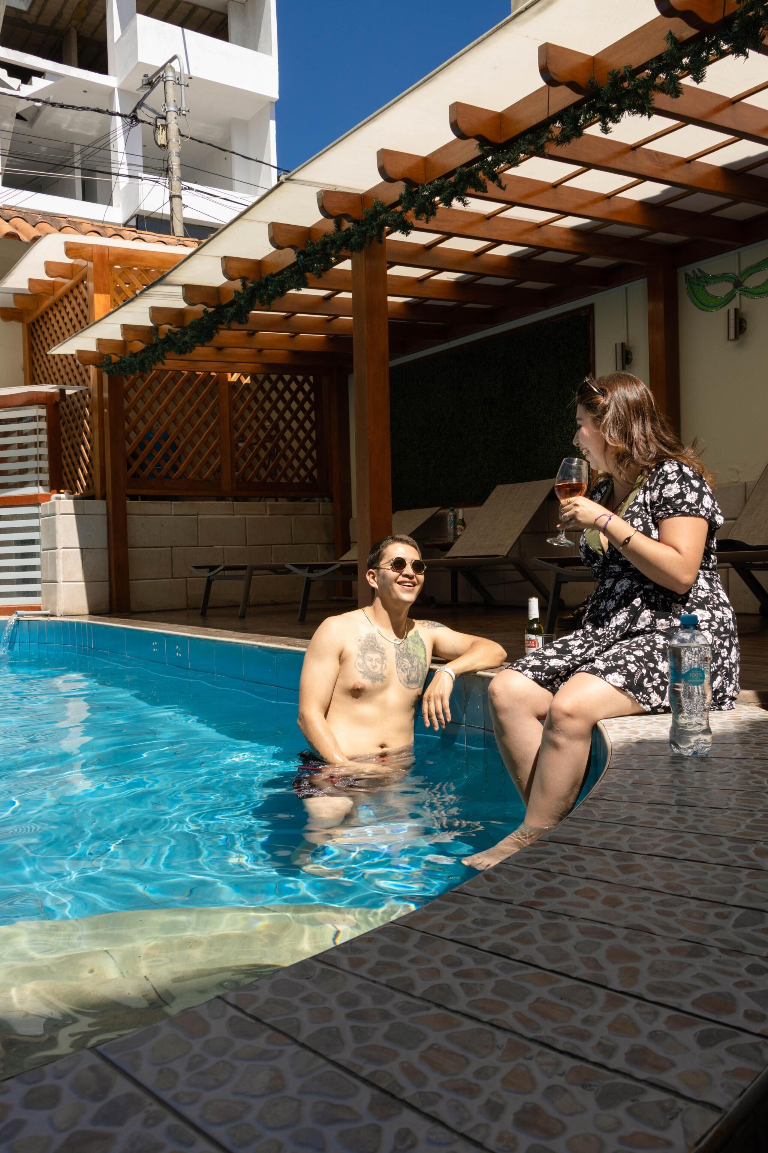 Un área de piscina con una pérgola de madera, sillas de descanso y un suelo de baldosas.