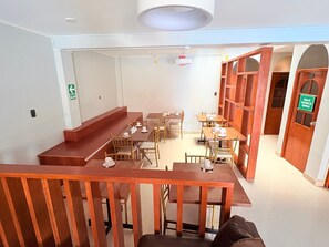 A cafe with wooden tables and chairs, a staircase, and a sign indicating a storage area. - Baños del Inca Hotel (Baños del Inca)
