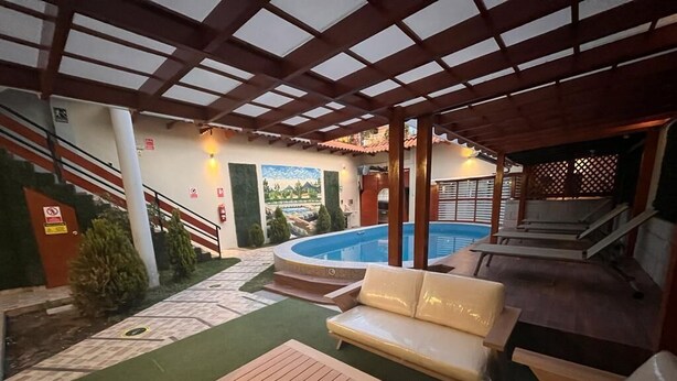 A pool area with a wooden deck, a white sofa, and a cushioned bench. - Baños del Inca Hotel (Baños del Inca)