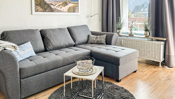 Een moderne woonkamer met een grijze modulaire bank, een klein bijzettafeltje en een ingelijst schilderij aan de muur.