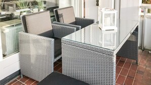 Een glazen tafel met vier grijze rieten stoelen, elk voorzien van een kussen.