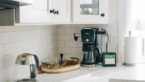 Una cocina con armarios blancos, una cafetera, una jarra de vidrio y un hervidor de agua.
