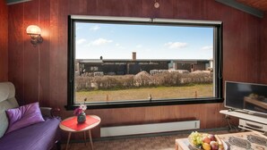 A room with a large window, wooden walls, a sofa, a small table with a vase, and a television. - 1 bedroom awesome home in Kalundborg (Kalundborg)