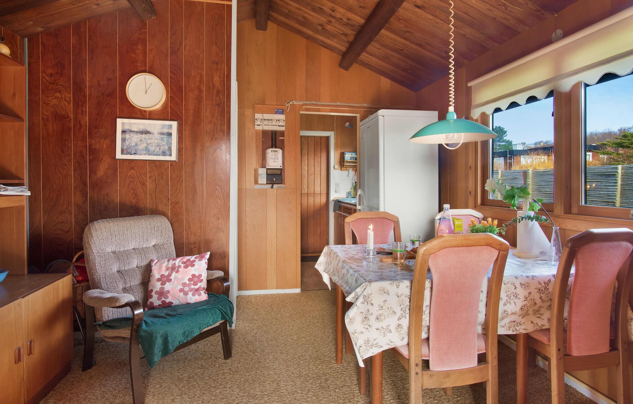 A cozy cabin interior with a wooden dining table, chairs, a sofa, and a clock on the wall.