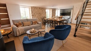 Uma sala de estar moderna com sofá, duas poltronas, uma mesa de centro e uma área de jantar com cadeiras e mesa.