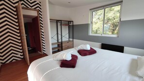 Quarto de hotel com uma cama, duas toalhas, uma janela com vista para árvores, um guarda-roupa e uma parede com padrão em Chevron.