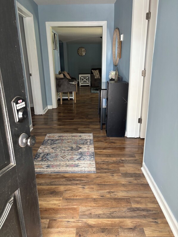 A hallway with wooden flooring, a patterned rug, and a door with a keypad lock. - Charming, spacious and updated 3 bedroom bungalow in up and coming Rocky Mount. (Rocky Mount)