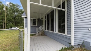 Ein Haus mit überdachter Veranda, sichtbarer Treppe und umzäunter Gartenfläche.