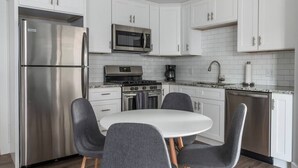 Una cocina moderna con armarios blancos, electrodomésticos de acero inoxidable, una mesa de comedor blanca con sillas y un backsplash de azulejos.