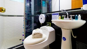 A modern bathroom with a white toilet, a glass shower enclosure, a sink with a soap dispenser, and a blue and white water bottle. - Ayenda 1067 Bogota Elite (Bogotá)
