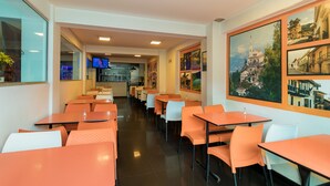 A restaurant with orange tables and chairs, a kitchen area in the background, and a large cityscape painting on the wall. - Ayenda 1067 Bogota Elite (Bogotá)