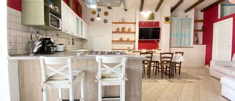A modern kitchen with a central island, white bar stools, and a dining area with a white table and chairs.