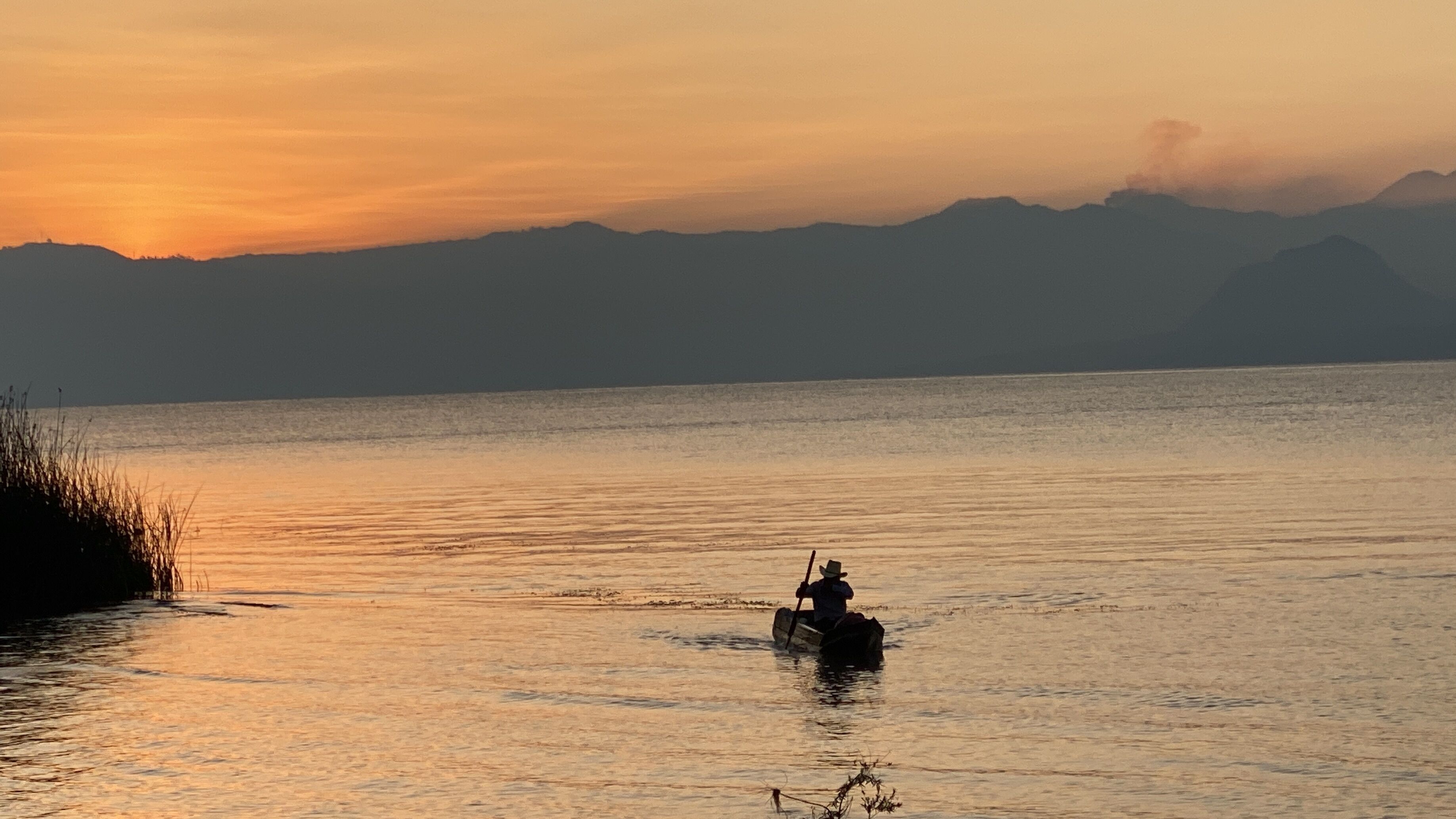 A calm lake at sunset with a silhouette of a person rowing a boat.