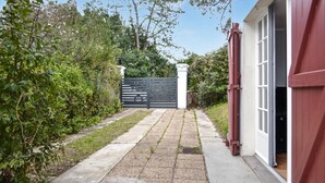 Un chemin pavé mène à une entrée fermée par un portail, avec une clôture blanche et une porte rouge.