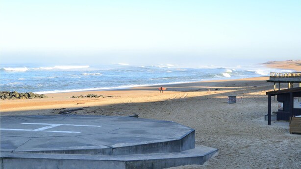 Une plage avec une plateforme d’observation en béton, un poste de surveillance pour les sauveteurs et une structure en bois sur la droite.
