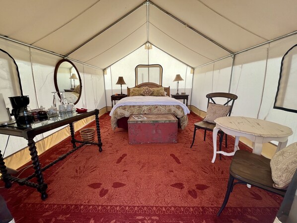 A tented room with a bed, a table with a coffee maker, a chair, and a small table with a lamp. - Beautiful Glamping Tent at Zenzen Gardens (Paonia)