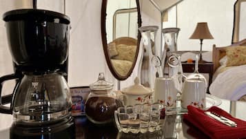 A coffee maker, a tea sampler, a glass jar, a set of glasses, and a red towel on a table in a hotel room.