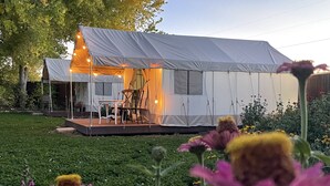 A tent with a dining area and a small stage, surrounded by greenery and flowers. - Beautiful Glamping Tent at Zenzen Gardens (Paonia)