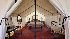 A tented room with a bed, bedside table, lamp, chair, and a mirror. - Beautiful Glamping Tent at Zenzen Gardens (Paonia)