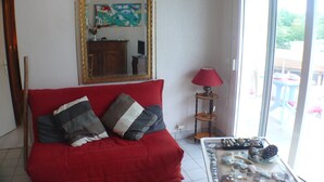 Un salon avec un canapé rouge, une table basse en verre ornée de pierres décoratives, une lampe rouge et un grand miroir au mur.