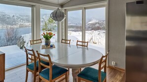 Een eetgedeelte met een ronde tafel, zes houten stoelen met blauwgroene kussens en een vaas met bloemen.