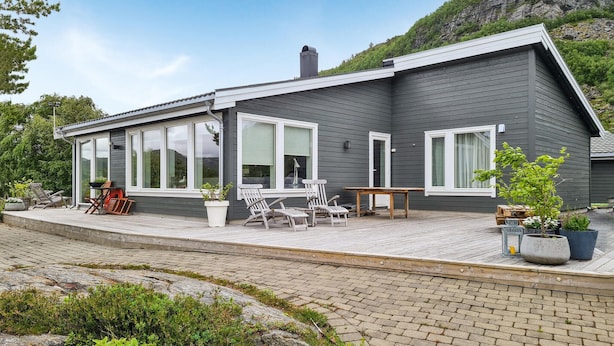 Een modern huis met een overdekte patio, grote ramen en een zitgedeelte buiten.