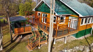 A wooden house with a green roof, a deck, and a small outdoor seating area.