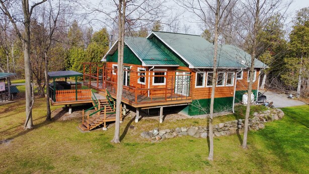 A wooden cabin with a green roof, a deck, and a stone wall.