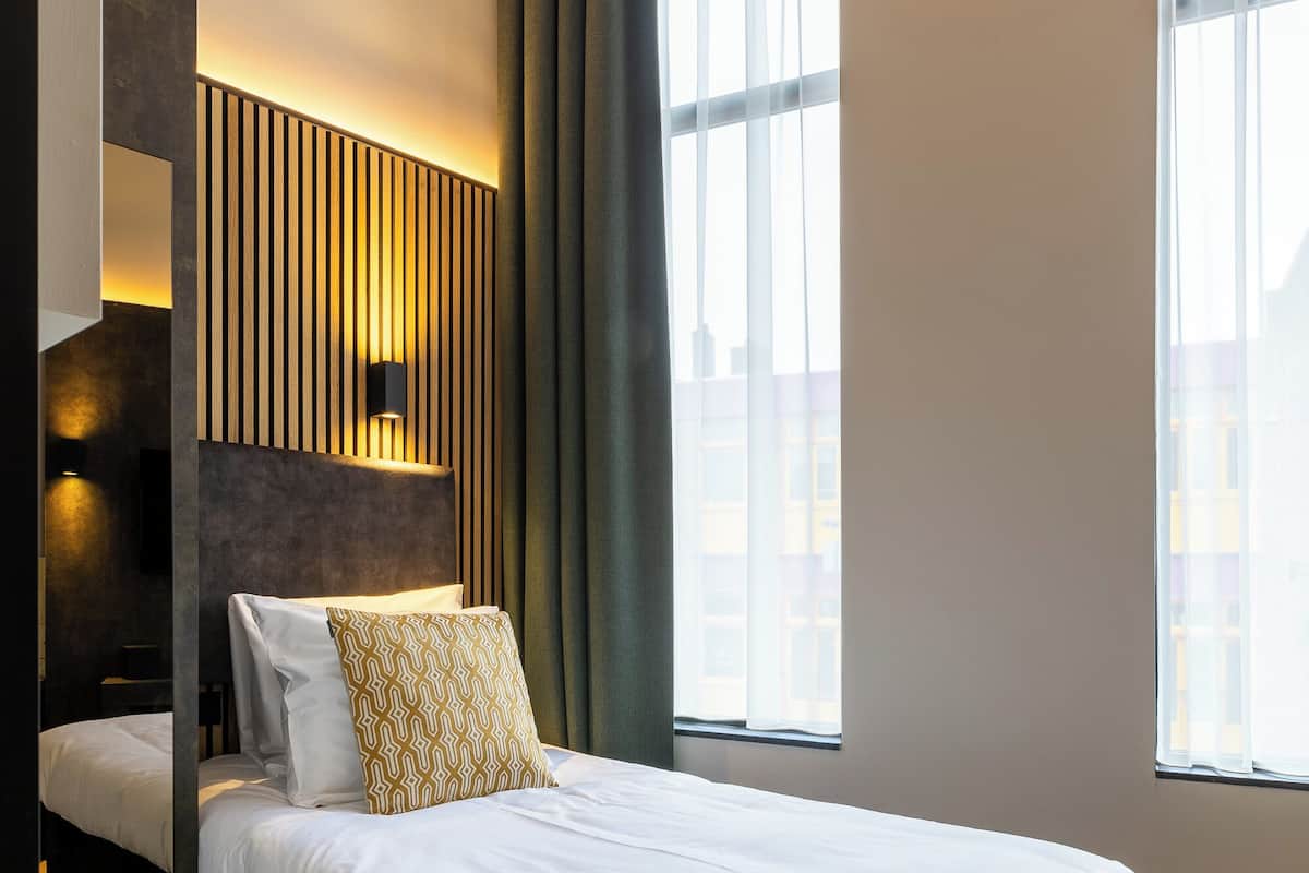 Una habitación de hotel moderna con una cama grande, una lámpara de pared y vistas a la ciudad a través de amplios ventanales.