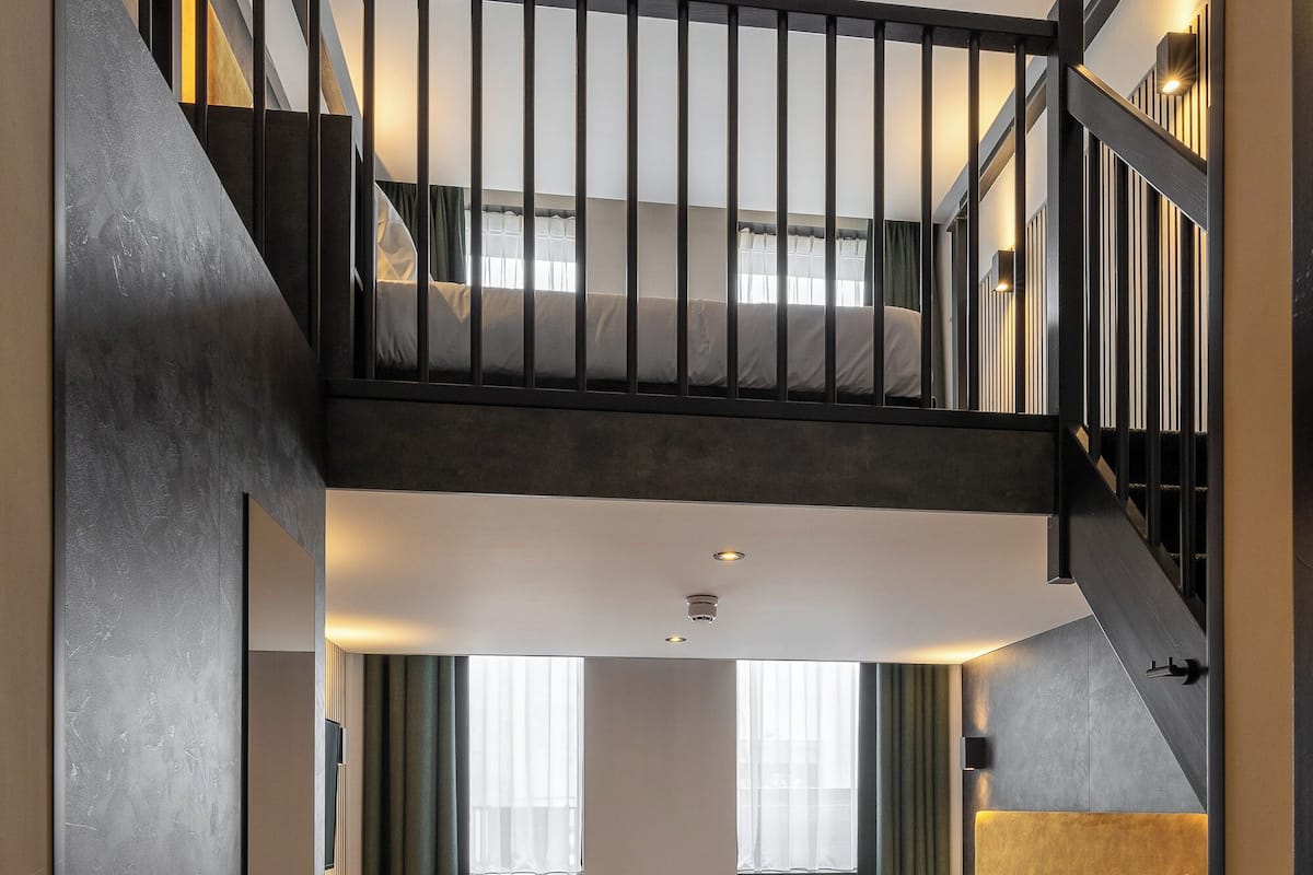 Un dormitorio tipo loft moderno con una cama grande, un escritorio y una escalera que lleva a un nivel superior.