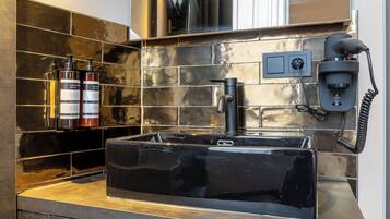 A modern bathroom with a black sink, a hairdryer, and two bottles of shampoo.