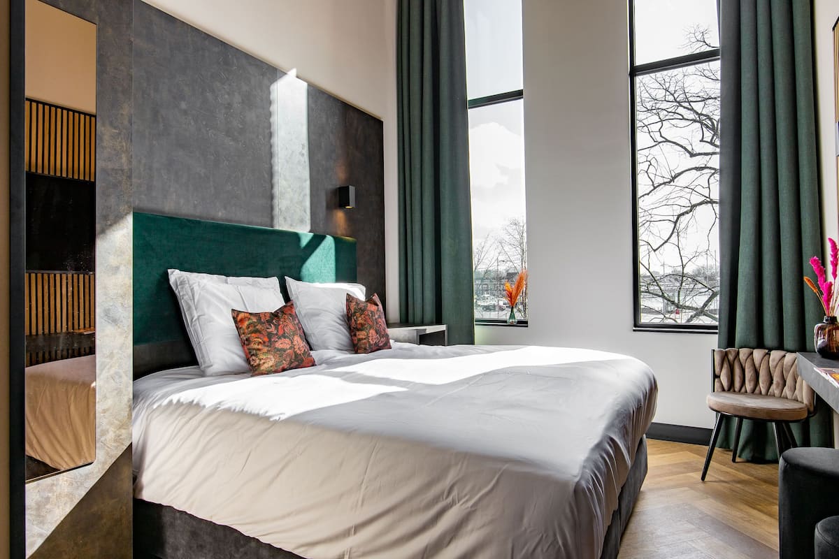 Una habitación de hotel moderna con una cama grande, un escritorio y vistas de la ciudad a través de un ventanal amplio.