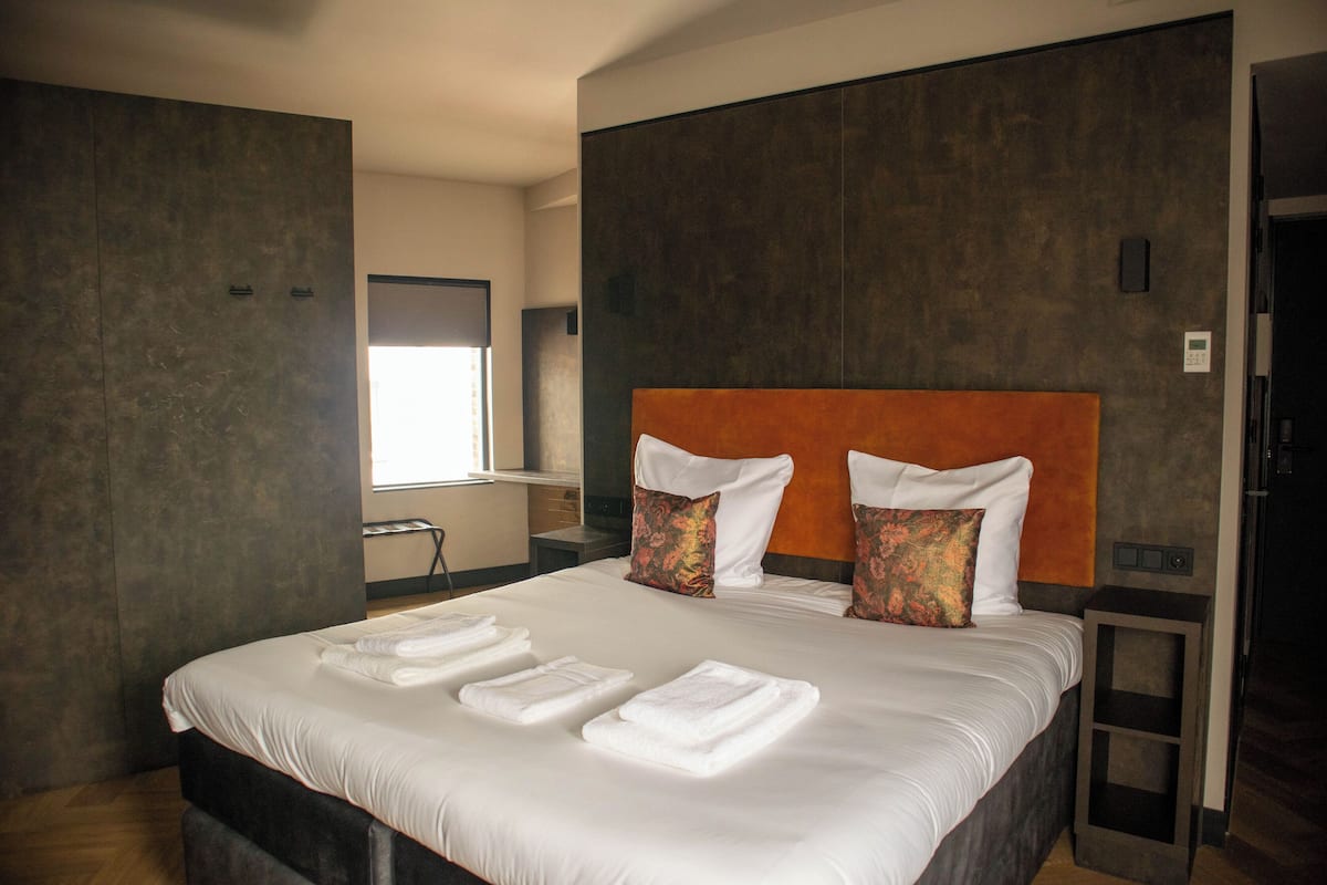 Una habitación de hotel moderna con una cama grande, dos almohadas y toallas dobladas con cuidado.