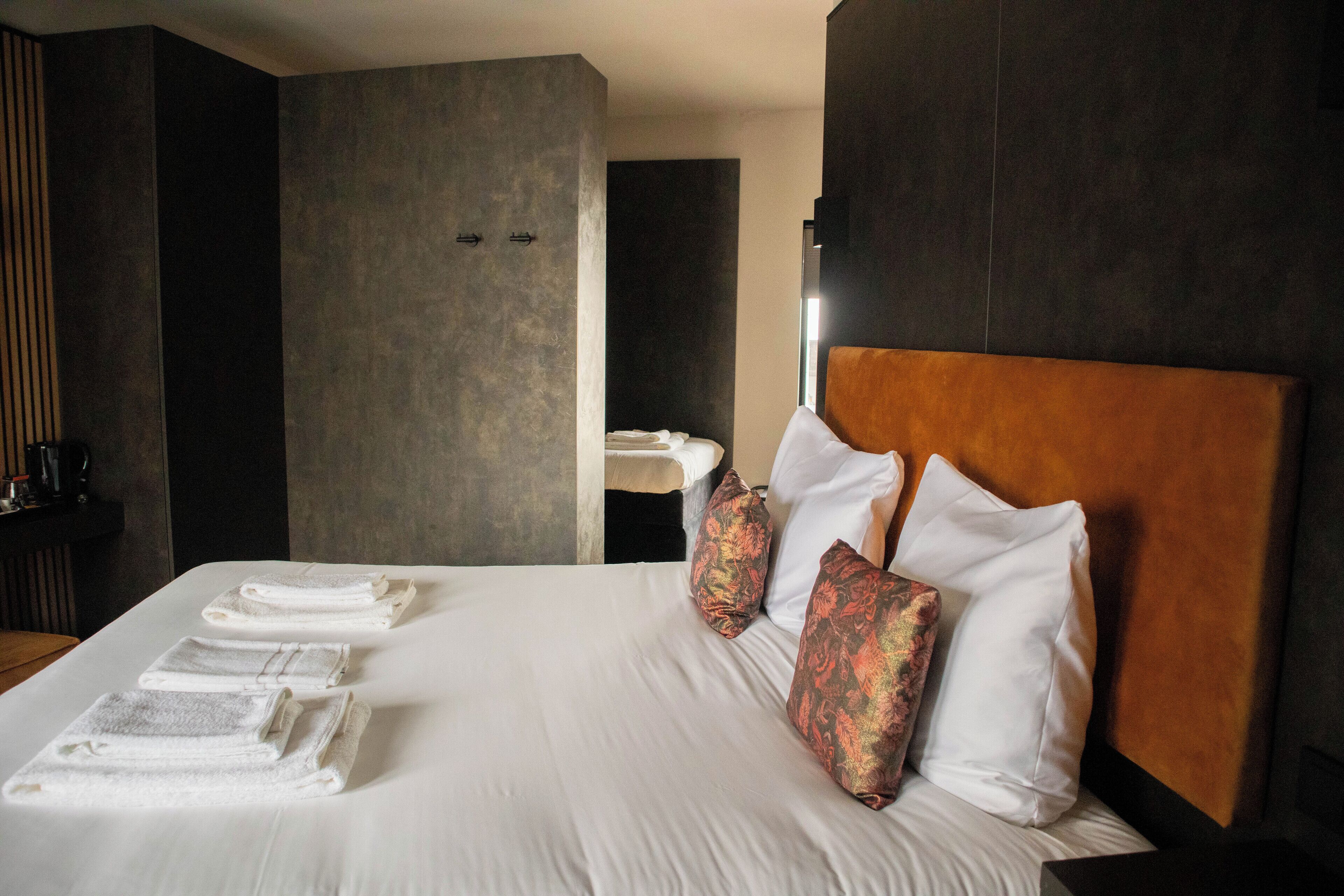 Une chambre d’hôtel avec un grand lit, des serviettes soigneusement pliées et une tête de lit en bois.