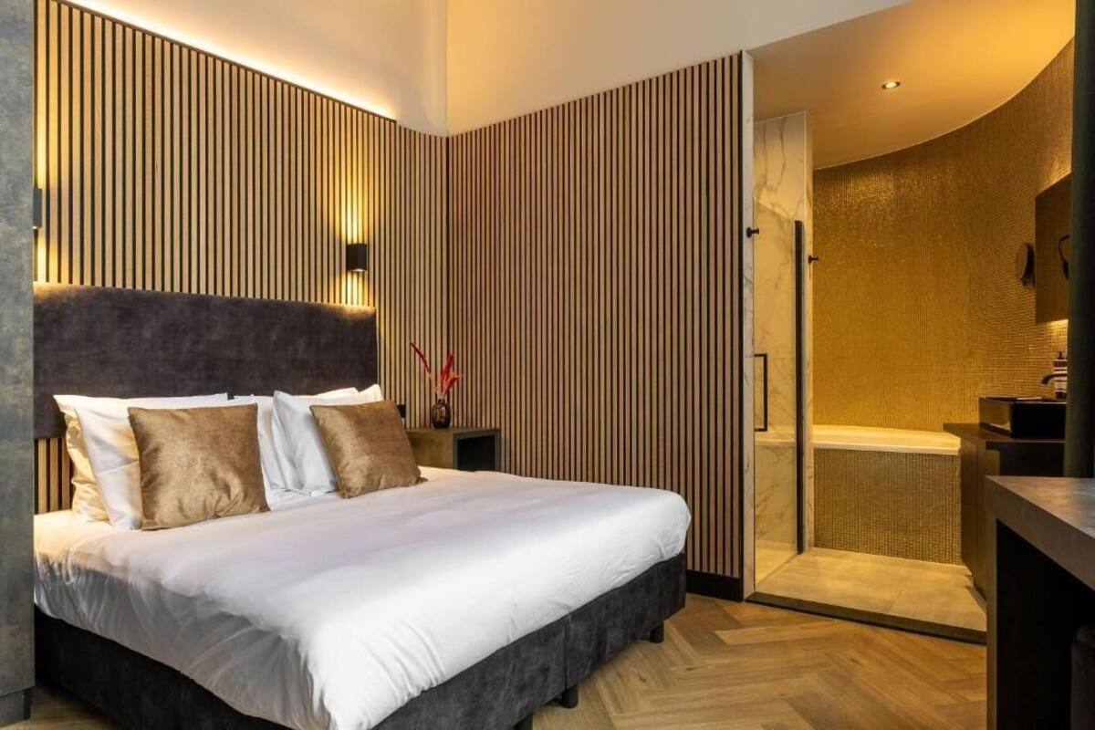 Habitación de hotel moderna con una cama grande, ducha a ras de suelo y pared de paneles de madera.