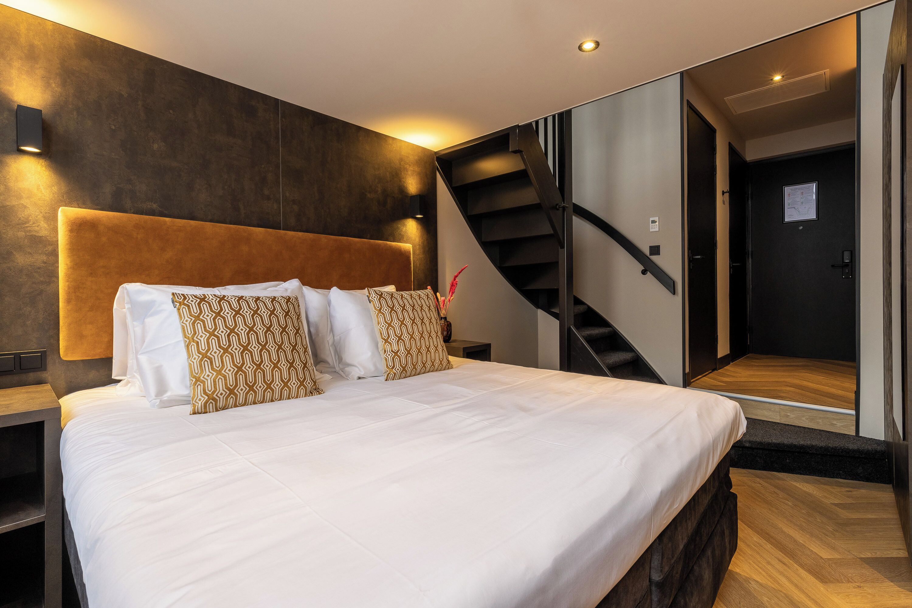 Un dormitorio moderno con una cama grande, cabecera, mesita de noche y una escalera.