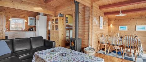 A cozy cabin interior with a sofa, dining table, and a wood-burning stove.