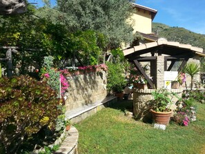 A garden with a stone wall, potted plants, and a wooden pergola. - Agriturismo L'uliveto (Reitano)