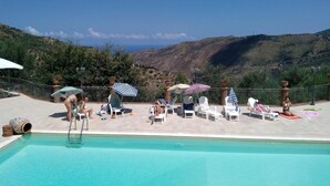 A pool area with lounge chairs and umbrellas, overlooking a mountainous landscape. - Agriturismo L'uliveto (Reitano)