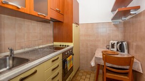 Una cocina compacta con lavamanos, estufa y una mesita pequeña con una tetera y una cesta.
