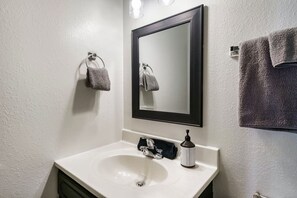 Een badkamer met een witte wasbak, een spiegel en twee handdoeken aan haken.